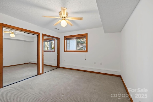 unfurnished bedroom with multiple closets, light colored carpet, a ceiling fan, a textured ceiling, and baseboards