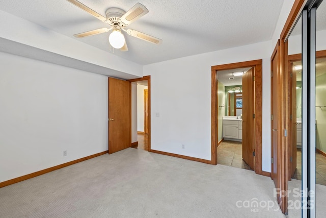 unfurnished bedroom featuring a textured ceiling, connected bathroom, light colored carpet, a ceiling fan, and baseboards