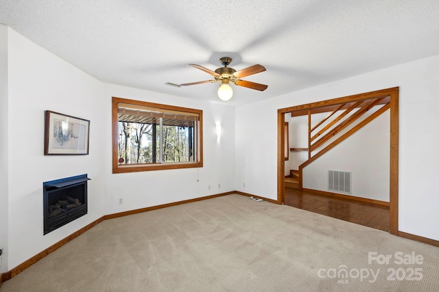 unfurnished living room with carpet, a fireplace, visible vents, a textured ceiling, and baseboards