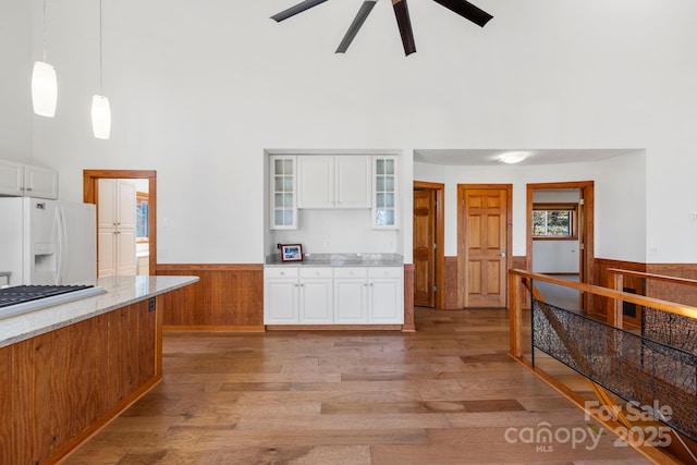 kitchen featuring white cabinets, a wainscoted wall, glass insert cabinets, decorative light fixtures, and white fridge with ice dispenser