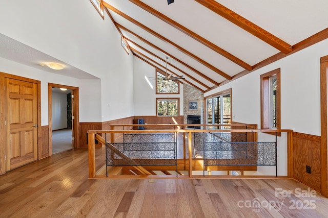 dining area with beam ceiling, a wainscoted wall, a fireplace, wood finished floors, and high vaulted ceiling