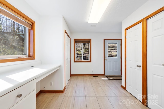 corridor featuring baseboards, light tile patterned floors, and a healthy amount of sunlight