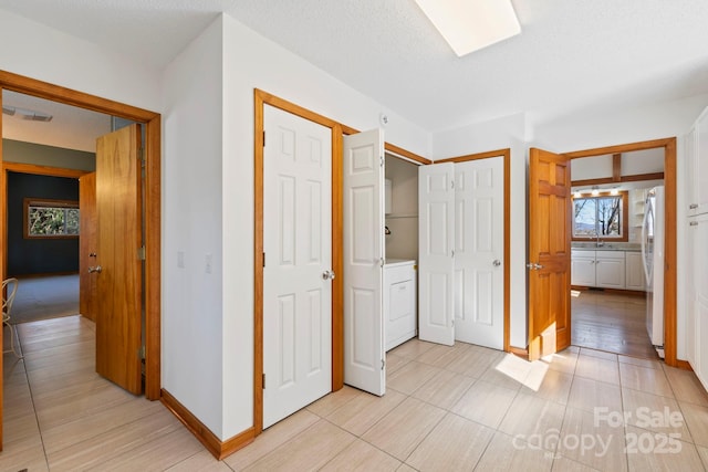 corridor with visible vents, a sink, a textured ceiling, washer / dryer, and baseboards