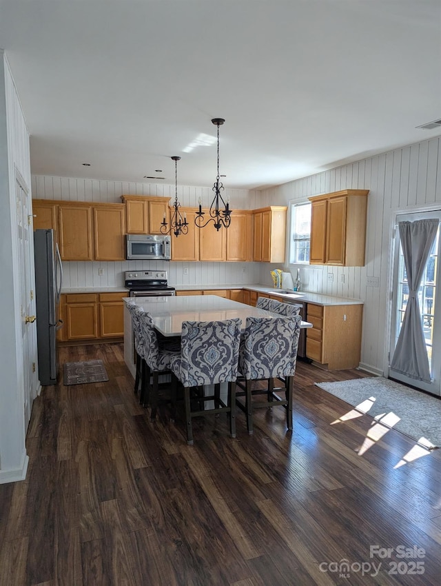 kitchen with appliances with stainless steel finishes, a center island, dark wood-style flooring, and light countertops