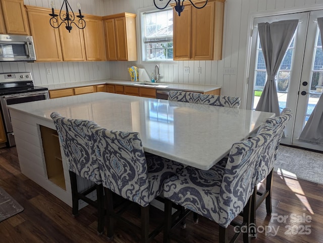 kitchen featuring stainless steel appliances, a breakfast bar, a sink, light countertops, and dark wood-style floors