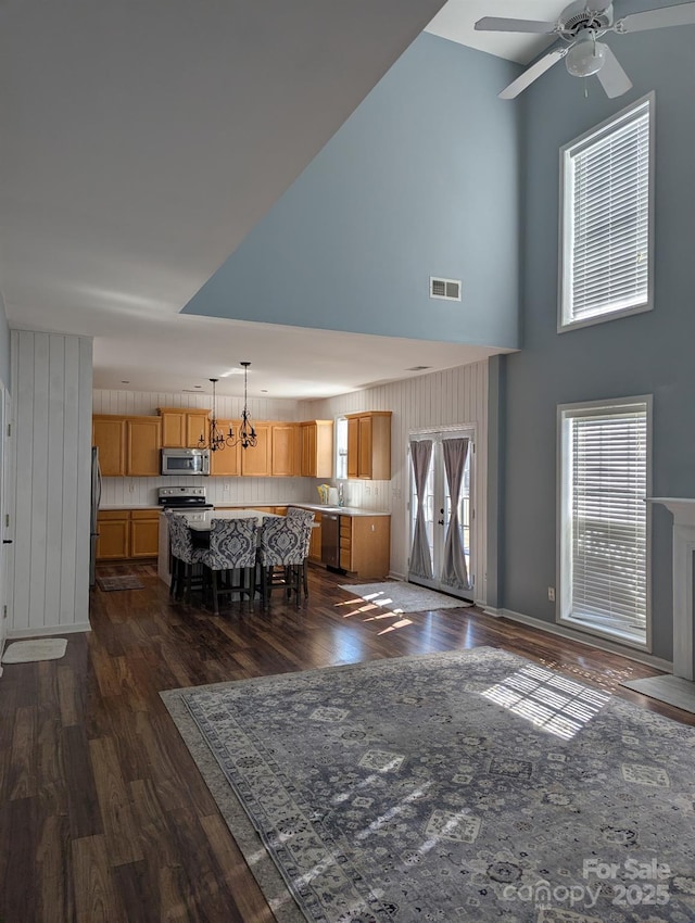 unfurnished dining area with dark wood-type flooring, visible vents, a high ceiling, and ceiling fan with notable chandelier