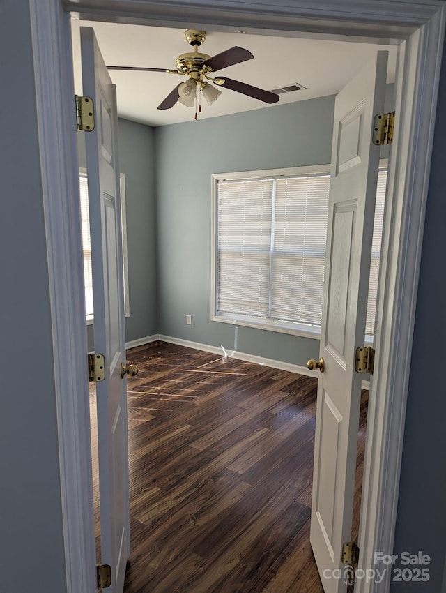 empty room featuring dark wood-style floors, a ceiling fan, visible vents, and baseboards