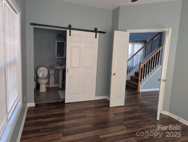 unfurnished bedroom with dark wood-type flooring, multiple windows, and a barn door