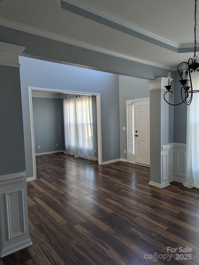 unfurnished living room with a chandelier, dark wood finished floors, crown molding, and baseboards