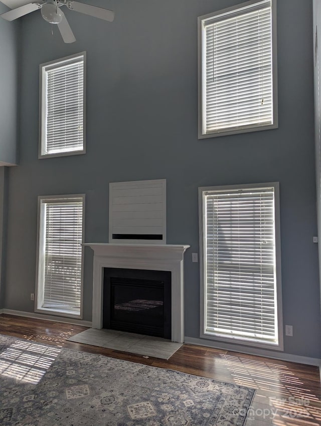 unfurnished living room featuring wood finished floors, a fireplace with flush hearth, a towering ceiling, and baseboards