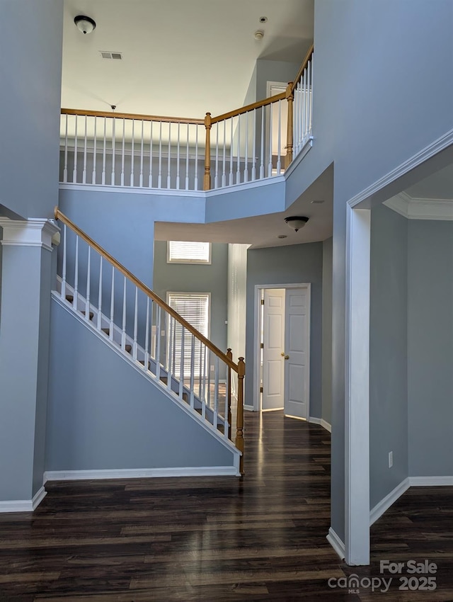 stairs featuring visible vents, a towering ceiling, baseboards, and wood finished floors