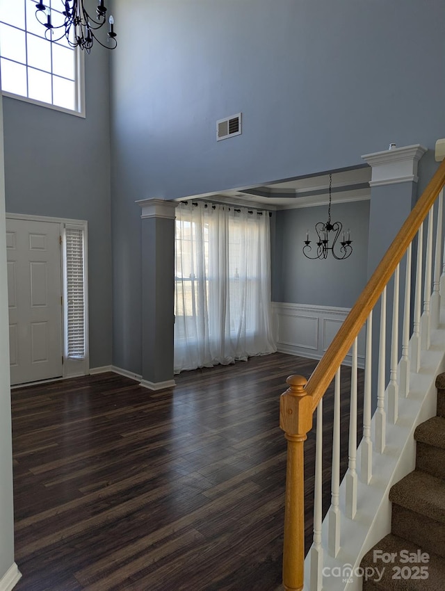 entryway with a wainscoted wall, dark wood finished floors, visible vents, stairway, and an inviting chandelier