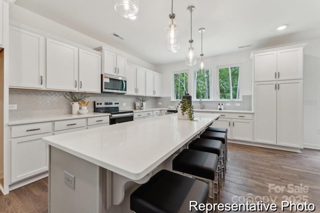 kitchen with appliances with stainless steel finishes, a center island, light countertops, white cabinetry, and backsplash