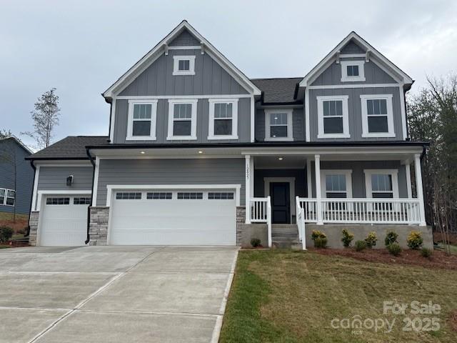 craftsman-style home with a front yard, an attached garage, covered porch, concrete driveway, and board and batten siding