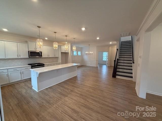 kitchen featuring dark wood-style floors, stainless steel microwave, black gas range, and light countertops