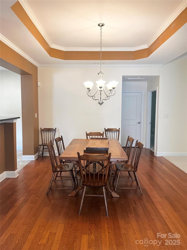 dining room featuring ornamental molding, a tray ceiling, wood-type flooring, baseboards, and a chandelier