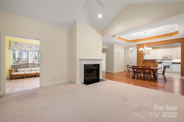 living room with a tray ceiling, light carpet, a fireplace with flush hearth, and ceiling fan with notable chandelier