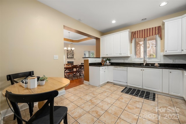 kitchen with white dishwasher, a sink, decorative backsplash, dark countertops, and a chandelier