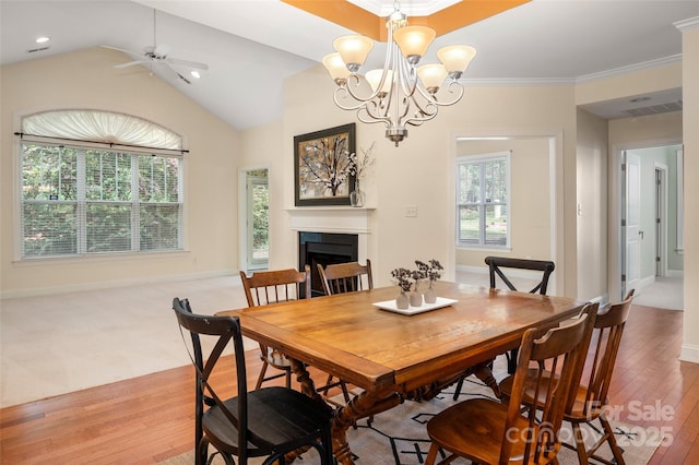 dining area with visible vents, light wood finished floors, a fireplace, crown molding, and ceiling fan with notable chandelier