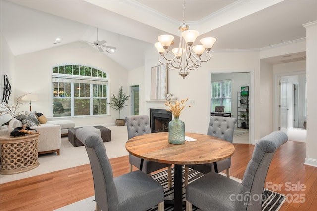 dining area with wood finished floors, ornamental molding, ceiling fan with notable chandelier, a fireplace, and lofted ceiling