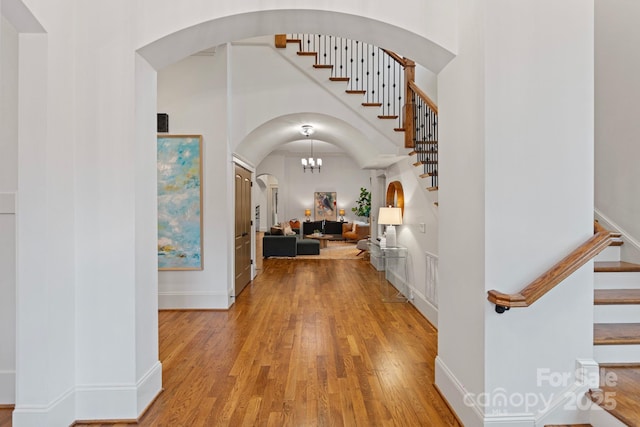 hall featuring a high ceiling, stairway, light wood-style floors, and arched walkways