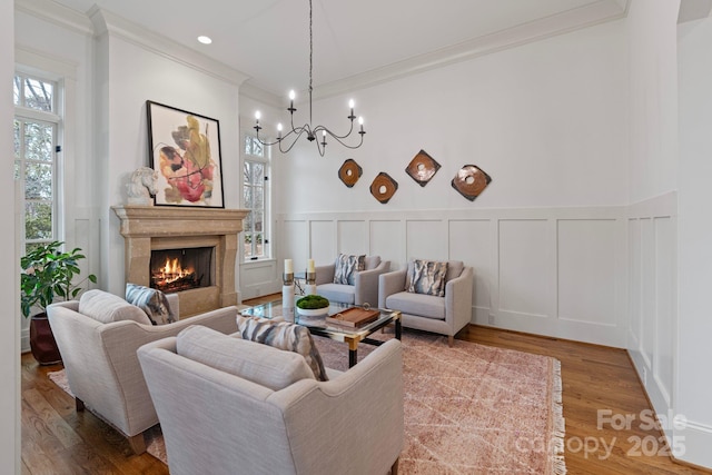 living room featuring wood finished floors, a premium fireplace, crown molding, a decorative wall, and a chandelier