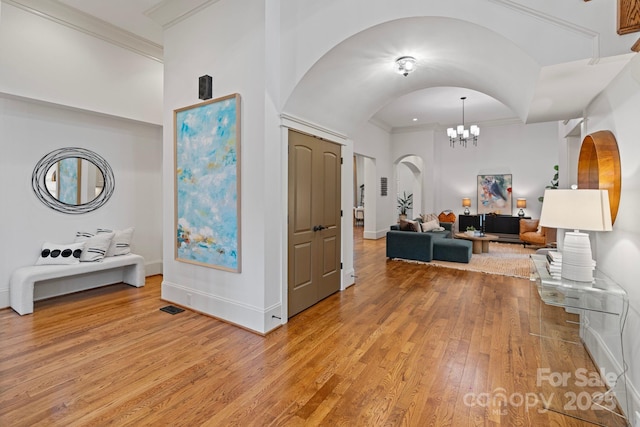 hallway with visible vents, arched walkways, light wood-style floors, crown molding, and a notable chandelier