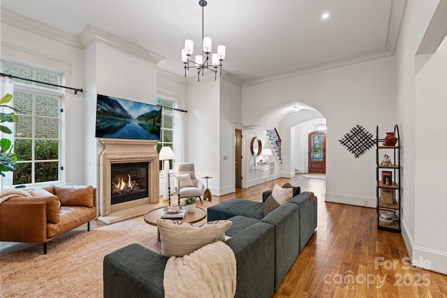 living area featuring baseboards, wood-type flooring, a glass covered fireplace, and ornamental molding