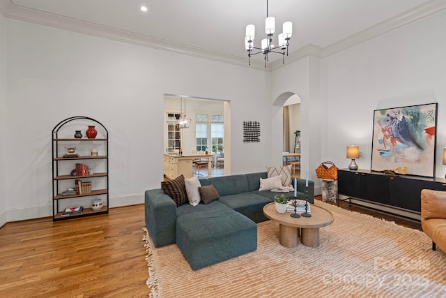 living area with a notable chandelier, ornamental molding, wood finished floors, arched walkways, and baseboards