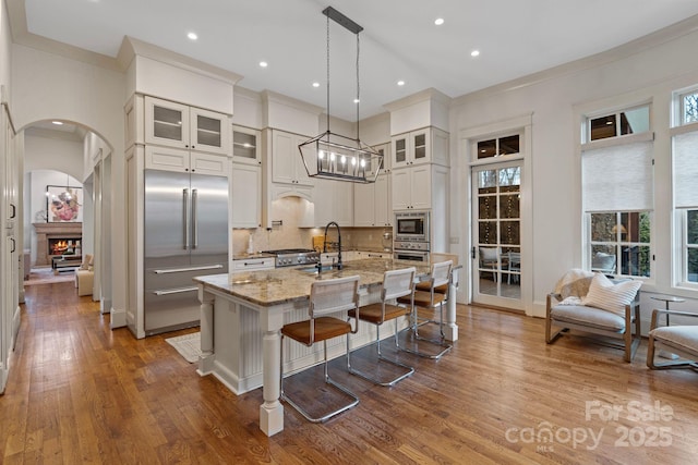 kitchen with light stone counters, backsplash, wood finished floors, a lit fireplace, and built in appliances