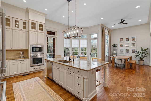 kitchen with light stone countertops, an island with sink, stainless steel appliances, decorative backsplash, and a sink