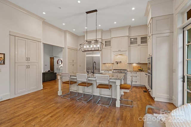 kitchen with backsplash, glass insert cabinets, an island with sink, a kitchen bar, and wood finished floors