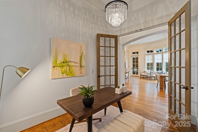 office area featuring wood finished floors, french doors, arched walkways, baseboards, and a chandelier