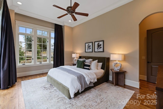 bedroom featuring wood finished floors, baseboards, arched walkways, and ornamental molding