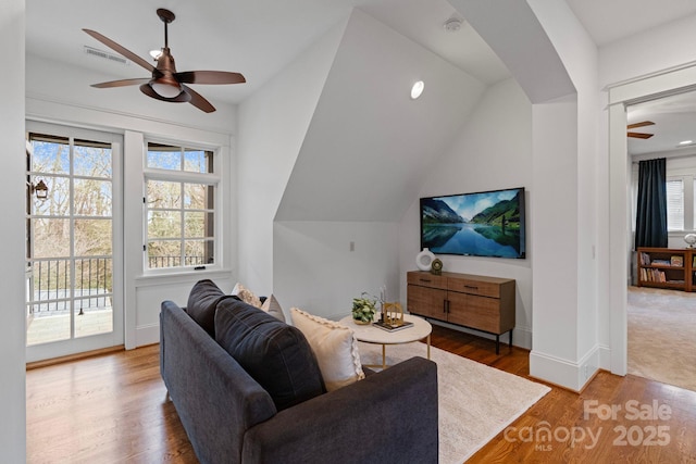 living area featuring visible vents, a ceiling fan, wood finished floors, baseboards, and vaulted ceiling