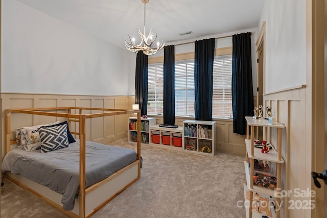 carpeted bedroom featuring visible vents, an inviting chandelier, and a wainscoted wall