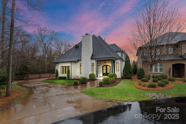 view of front of house with concrete driveway, stucco siding, a front yard, and a chimney