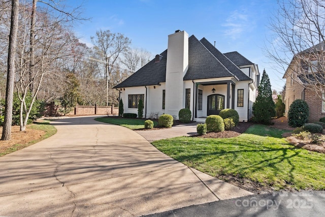 view of front of home featuring a shingled roof, a front lawn, driveway, and a chimney