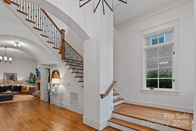 stairway featuring visible vents, ornamental molding, wood finished floors, baseboards, and a chandelier