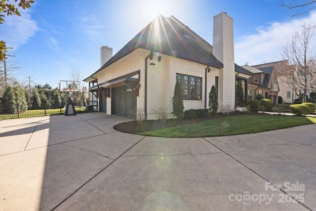 view of property exterior with concrete driveway, an attached garage, fence, and a chimney