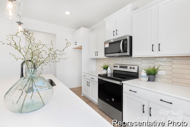 kitchen with light countertops, decorative backsplash, appliances with stainless steel finishes, white cabinets, and light wood-type flooring