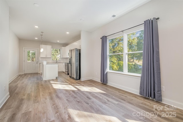 unfurnished living room with baseboards, a healthy amount of sunlight, visible vents, and light wood-style floors