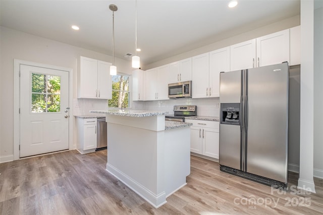 kitchen with hanging light fixtures, appliances with stainless steel finishes, white cabinetry, and a center island