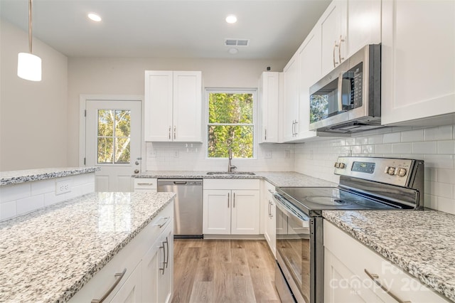 kitchen featuring stainless steel appliances, a sink, visible vents, white cabinets, and pendant lighting