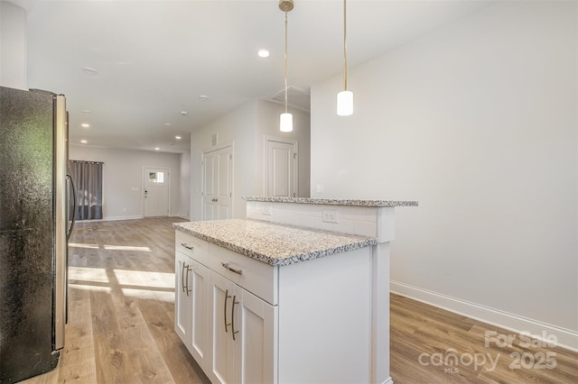 kitchen with white cabinets, a center island, decorative light fixtures, light stone countertops, and freestanding refrigerator