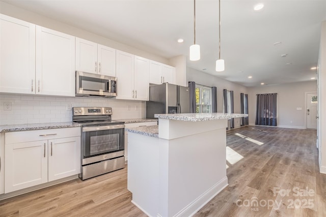 kitchen featuring stainless steel appliances, white cabinets, decorative light fixtures, and light stone counters