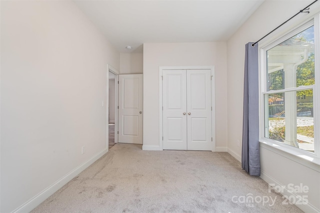 unfurnished bedroom featuring a closet, light colored carpet, and baseboards