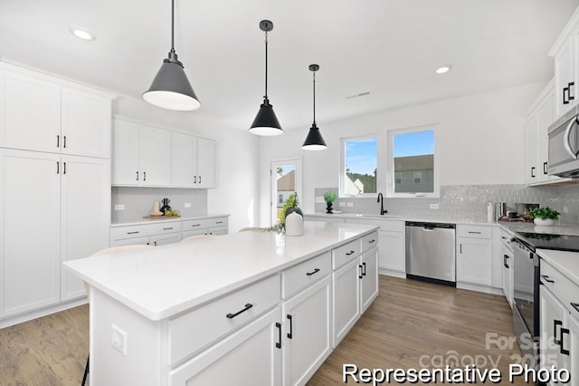 kitchen featuring appliances with stainless steel finishes, a center island, light countertops, white cabinetry, and pendant lighting