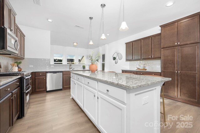 25966 Appleyard Ct Unit 1205, Lancaster, SC 29720 - kitchen with appliances with stainless steel finishes, tasteful backsplash, a center island, light stone countertops, and light wood-style floors