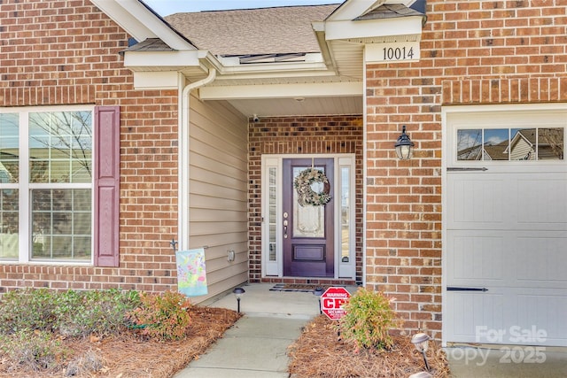 view of exterior entry with a garage, brick siding, and a shingled roof